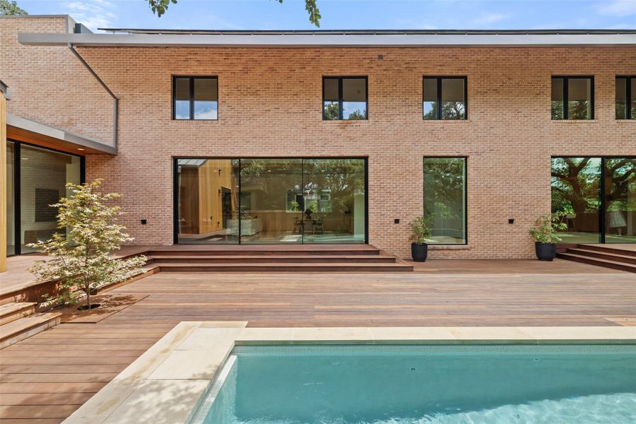 Rear view of house with a wooden deck, an outdoor pool, and brick siding