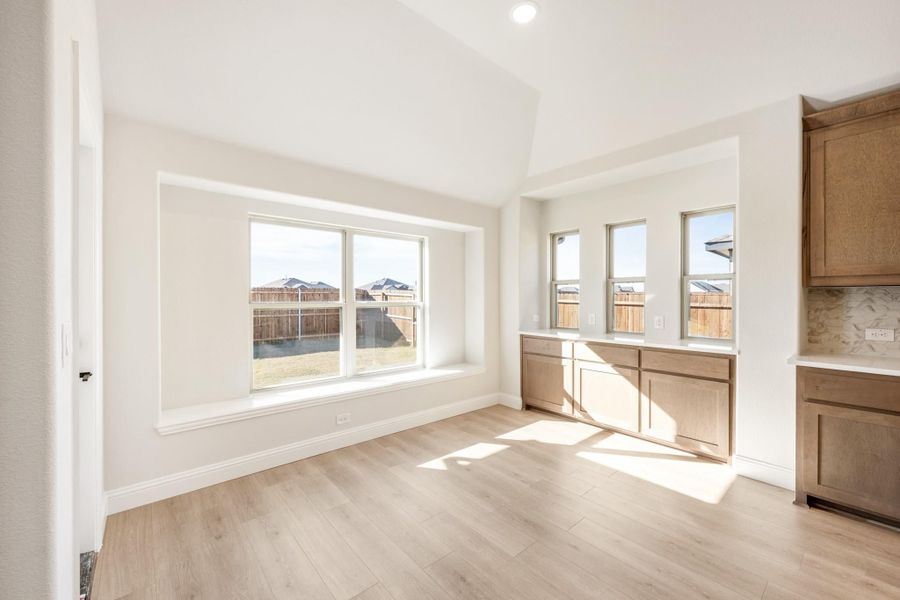 Open dining area with light wood floors, large windows, and adjacent kitchen cabinets with white countertops