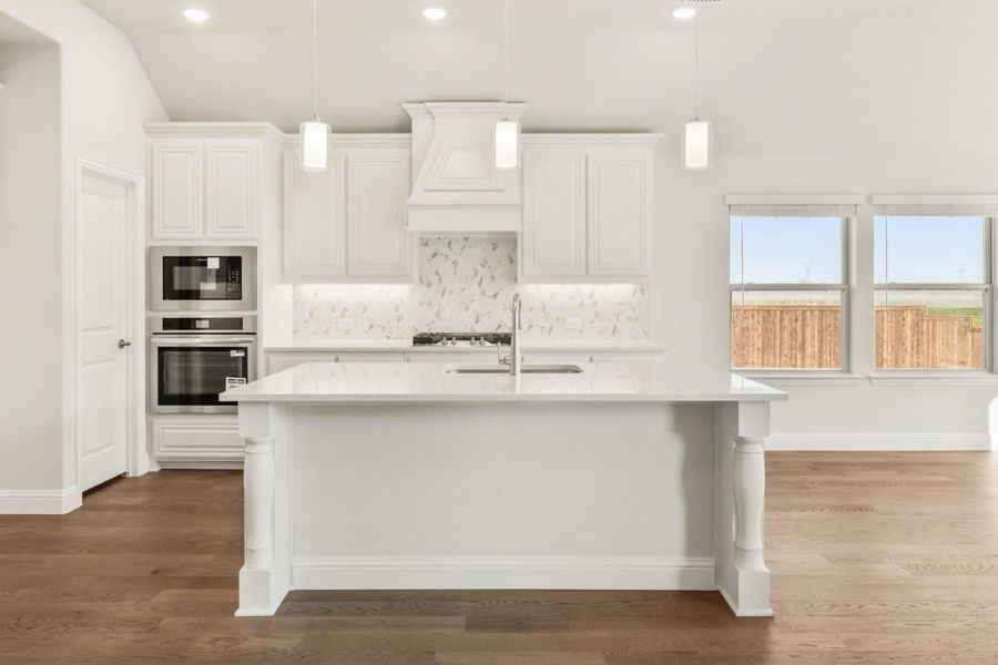 White kitchen with large island, stainless steel appliances, marble backsplash, and hardwood floors