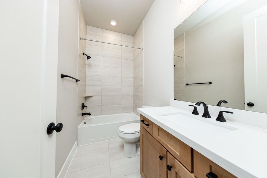 This secondary bathroom features a modern vanity, tub/shower combination with gorgeous tile surround, and modern black matte finishes.