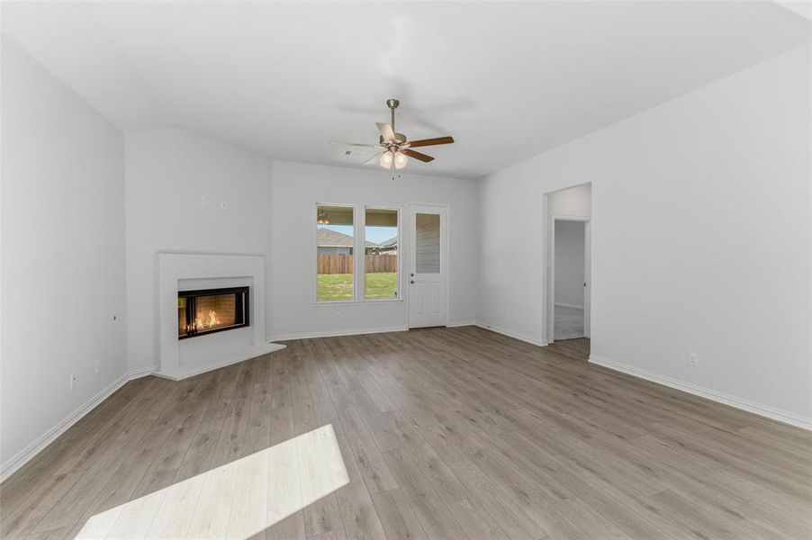 Unfurnished living room with a ceiling fan, a glass covered fireplace, and light wood finished floors