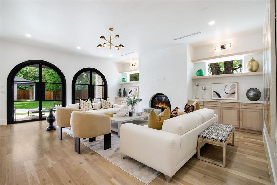 Living area showcasing light wood-finish flooring, a built-in fireplace, and two arched glass-paneled doors opening to the exterior Living area showcasing light wood-finish flooring, a built-in fireplace, and two arched glass-paneled doors opening to the exterior