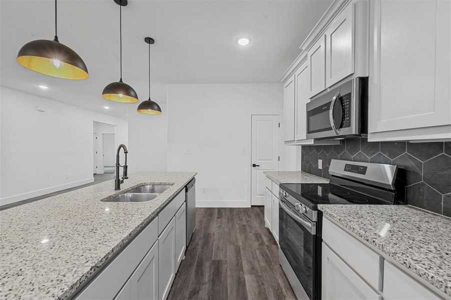 Kitchen featuring decorative light fixtures, stainless steel appliances, dark hardwood / wood-style flooring, sink, and white cabinets