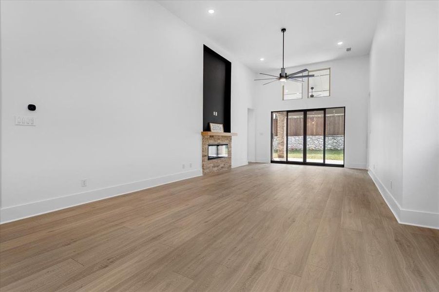 Unfurnished living room featuring a glass covered fireplace, light wood-style floors, a towering ceiling, ceiling fan, and recessed lighting