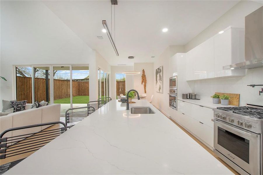 Kitchen with light stone counters, white cabinetry, high end stainless steel range, wall chimney exhaust hood, and decorative light fixtures