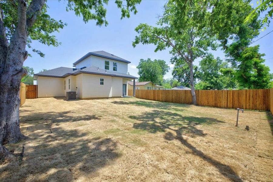 Spacious backyard featuring a new privacy fence, mature trees, and a two-story home with light-colored siding and a dark roof Spacious backyard featuring a new privacy fence, mature trees, and a two-story home with light-colored siding and a dark roof