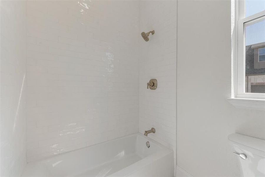 White subway tile surround with brushed nickel fixtures, a standard bathtub, and a window providing natural light White subway tile surround with brushed nickel fixtures, a standard bathtub, and a window providing natural light