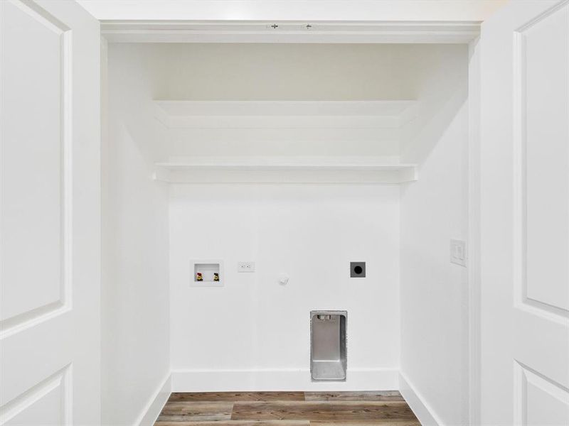 Dedicated laundry alcove featuring clean white walls, built-in shelving, wood-finish flooring, and essential utility hookups Dedicated laundry alcove featuring clean white walls, built-in shelving, wood-finish flooring, and essential utility hookups