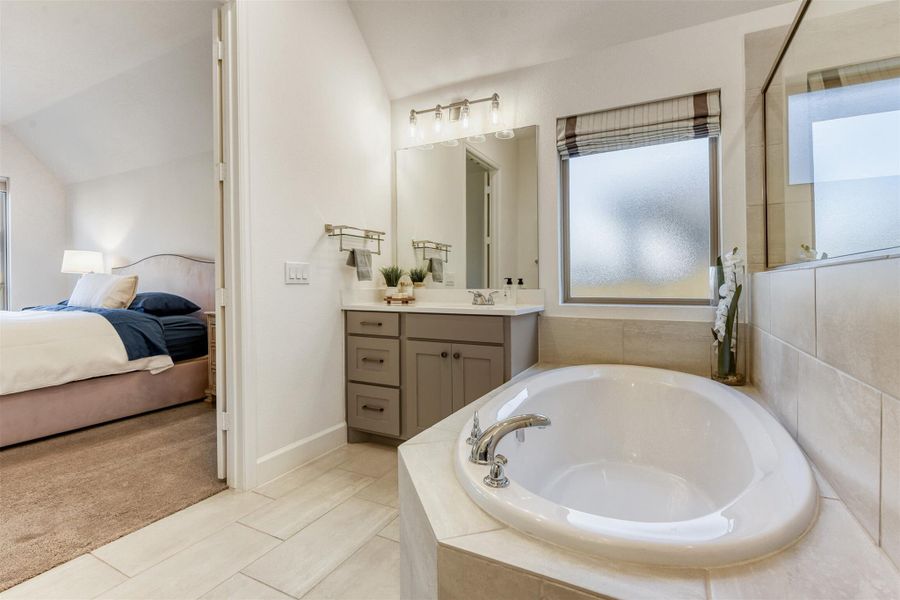 Ensuite bathroom with a bath, vanity, vaulted ceiling, light colored carpet, and light tile patterned floors