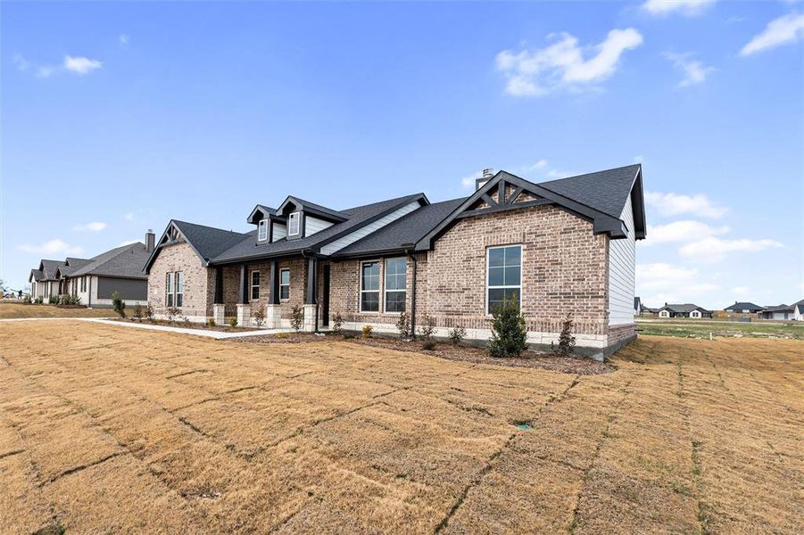 View of front of property with brick siding, covered porch, roof with shingles, and a front lawn