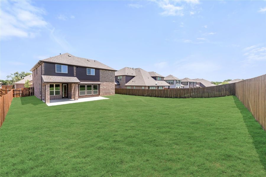 Two-story brick home with large fenced backyard, green lawn, and covered patio