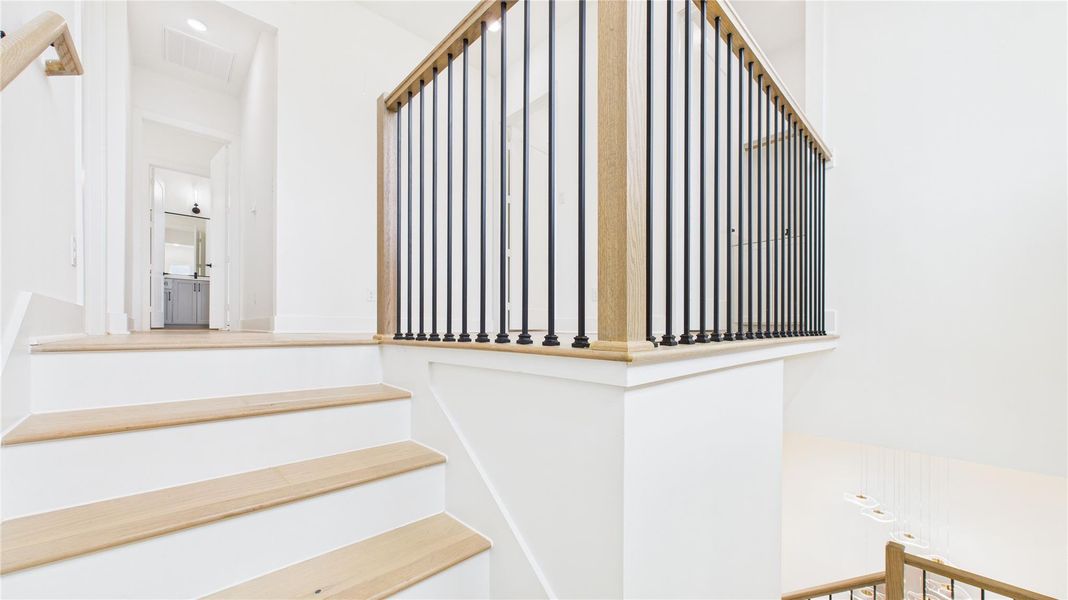 The open design leads to an upper landing with a glimpse into a hallway and a well-lit room in the background, creating an inviting and spacious feel.