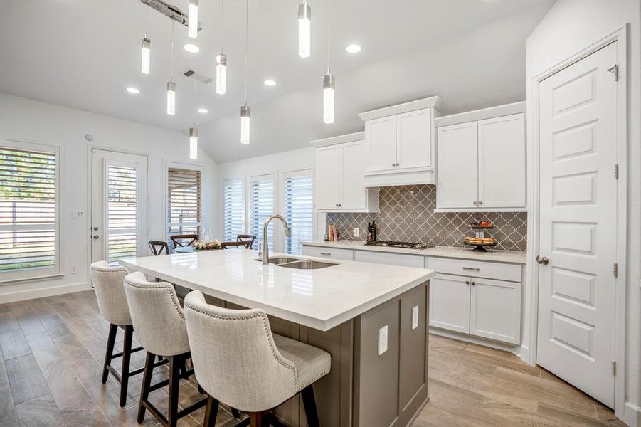 The kitchen has a modern aesthetic with white cabinetry, stainless steel appliances, and a central island with a sleek faucet and pendant lighting above.