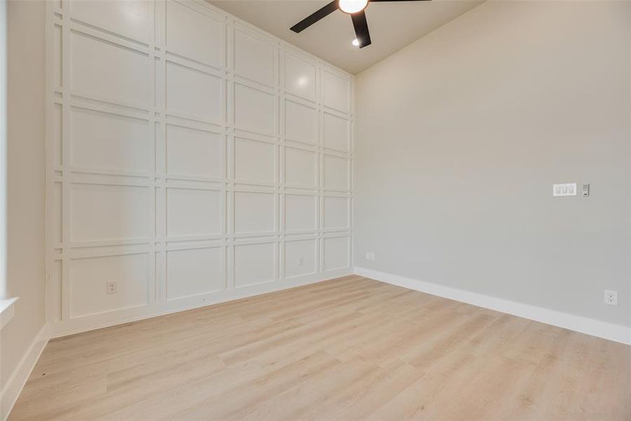 Empty room with a ceiling fan, light wood finished floors, and a decorative wall