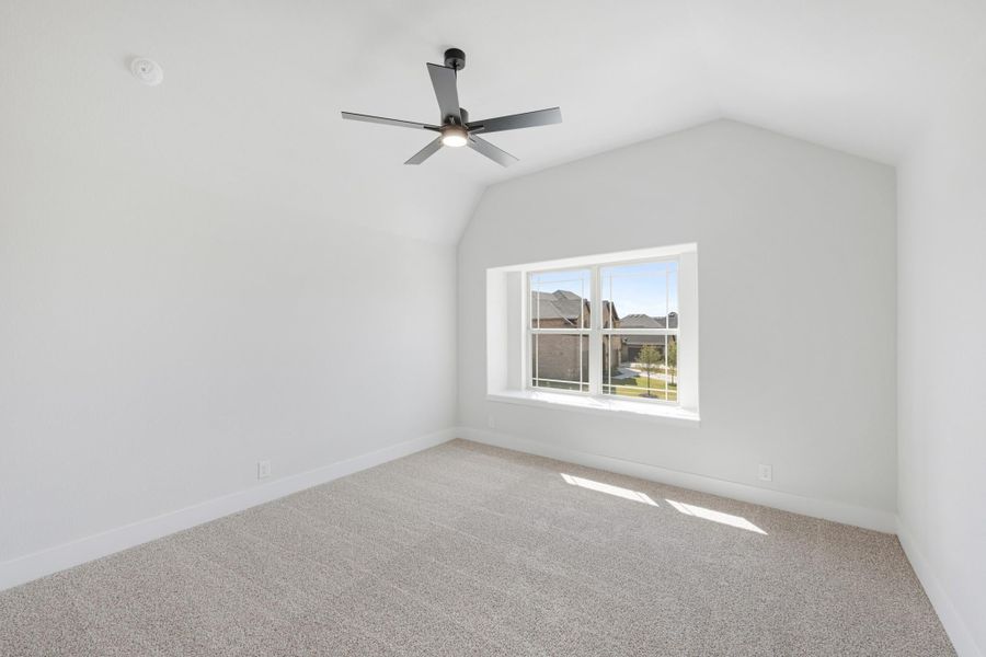 Empty bedroom with vaulted ceiling, ceiling fan, carpet flooring, and a single window with neighborhood view.