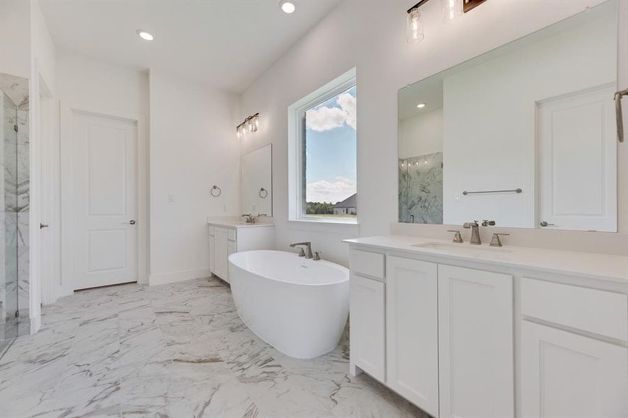 Full bath featuring light marble finish flooring, two vanities, a freestanding tub, a marble finish shower, and recessed lighting