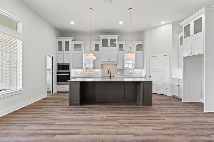 Kitchen featuring glass insert cabinets, tasteful backsplash, appliances with stainless steel finishes, white cabinets, and dark wood-style floors Kitchen featuring glass insert cabinets, tasteful backsplash, appliances with stainless steel finishes, white cabinets, and dark wood-style floors