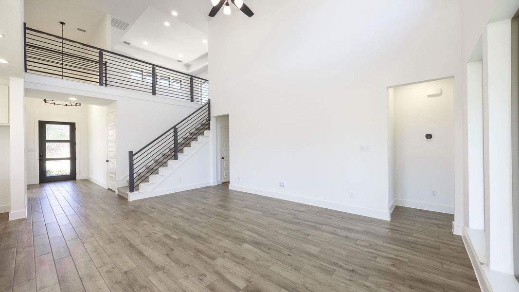 Unfurnished living room featuring a towering ceiling, wood finished floors, stairs, ceiling fan, and a chandelier