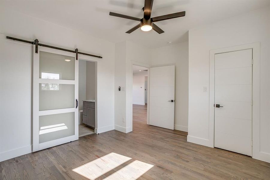 Unfurnished bedroom with light wood finished floors, ensuite bath, a ceiling fan, and a barn door Unfurnished bedroom with light wood finished floors, ensuite bath, a ceiling fan, and a barn door