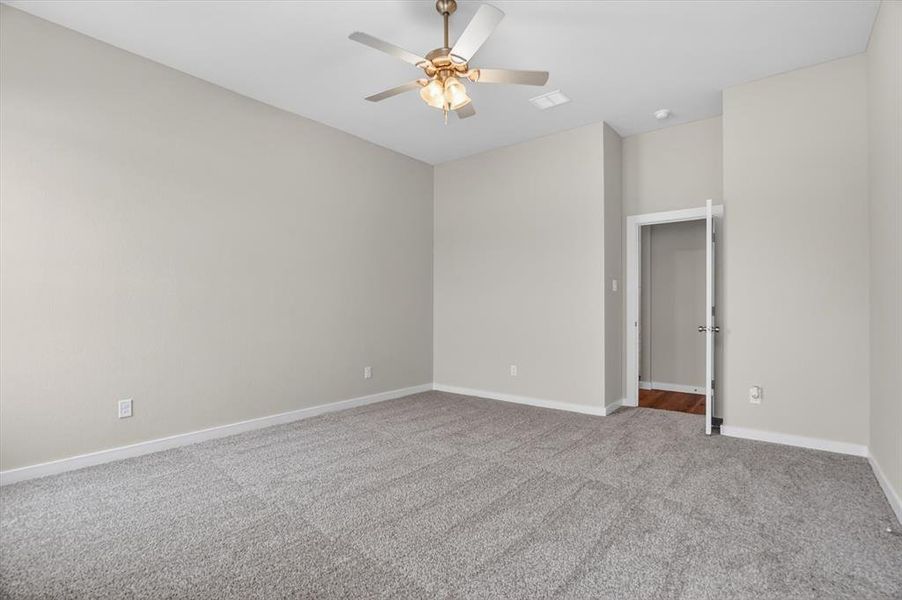 Spacious room featuring neutral wall tones, grey carpeting, a ceiling fan with integrated lighting, and white baseboards Spacious room featuring neutral wall tones, grey carpeting, a ceiling fan with integrated lighting, and white baseboards
