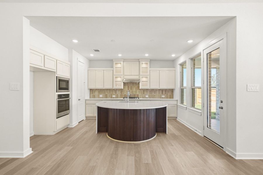 A bright and airy kitchen featuring a round-front island, ample cabinetry, and large windows that fill the space with natural light. A bright and airy kitchen featuring a round-front island, ample cabinetry, and large windows that fill the space with natural light.