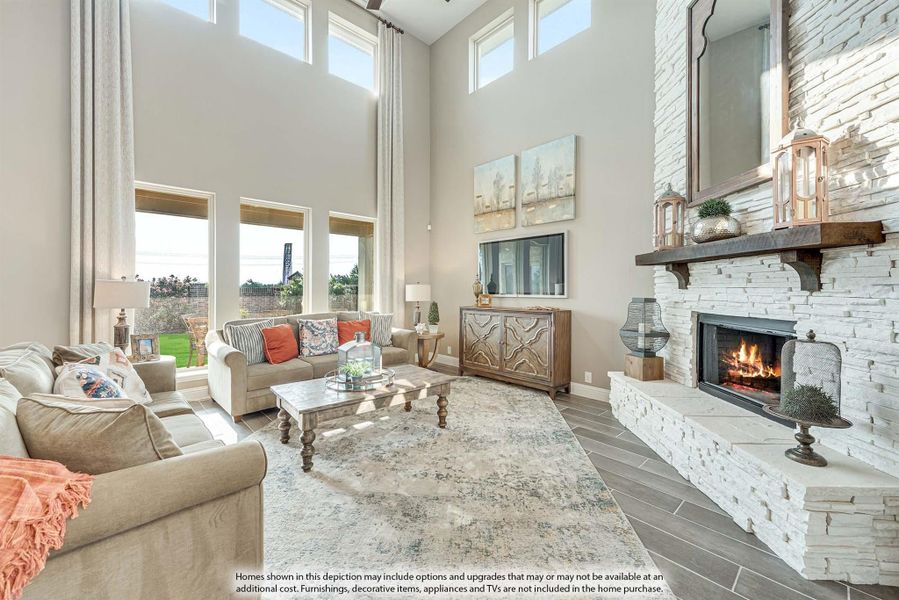 Living room with two-story ceiling, stone fireplace, and large windows overlooking backyard