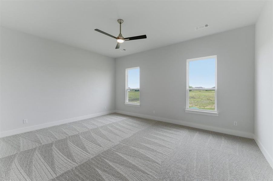 Spacious room featuring gray patterned carpeting, light gray walls, a ceiling fan with integrated lighting, and two windows with white trim