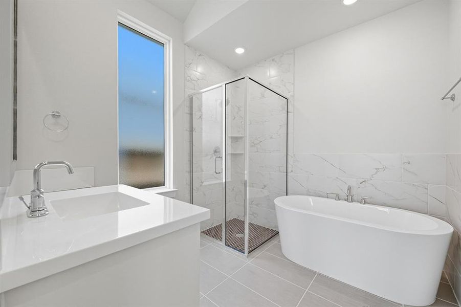 Full bathroom featuring vanity, a freestanding tub, a marble finish shower, tile walls, and light tile patterned flooring Full bathroom featuring vanity, a freestanding tub, a marble finish shower, tile walls, and light tile patterned flooring