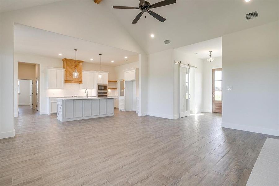 Unfurnished living room with light hardwood / wood-style flooring, sink, a barn door, high vaulted ceiling, and ceiling fan