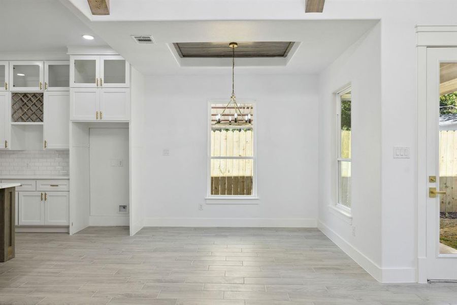 Unfurnished dining area featuring a chandelier, light hardwood / wood-style floors, and a raised ceiling