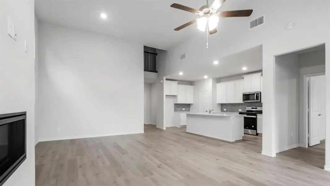 Unfurnished living room with light wood finished floors, a ceiling fan, recessed lighting, a glass covered fireplace, and a high ceiling Unfurnished living room with light wood finished floors, a ceiling fan, recessed lighting, a glass covered fireplace, and a high ceiling