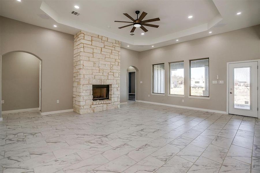 Unfurnished living room with a raised ceiling, a stone fireplace, ceiling fan, and a high ceiling