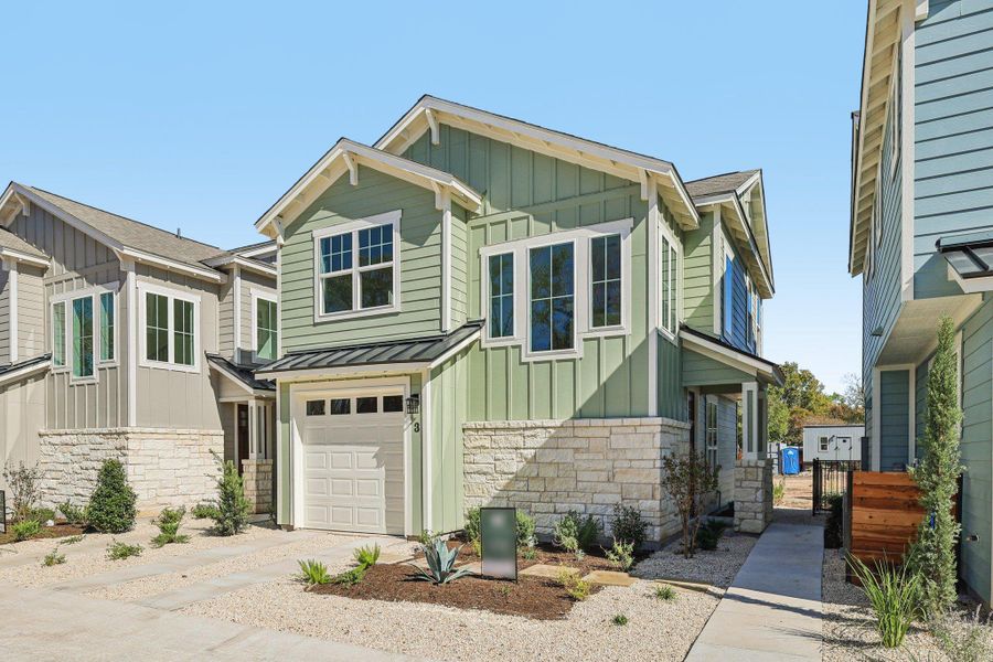 Craftsman house featuring stone siding, board and batten siding, an attached garage, a standing seam roof, and driveway