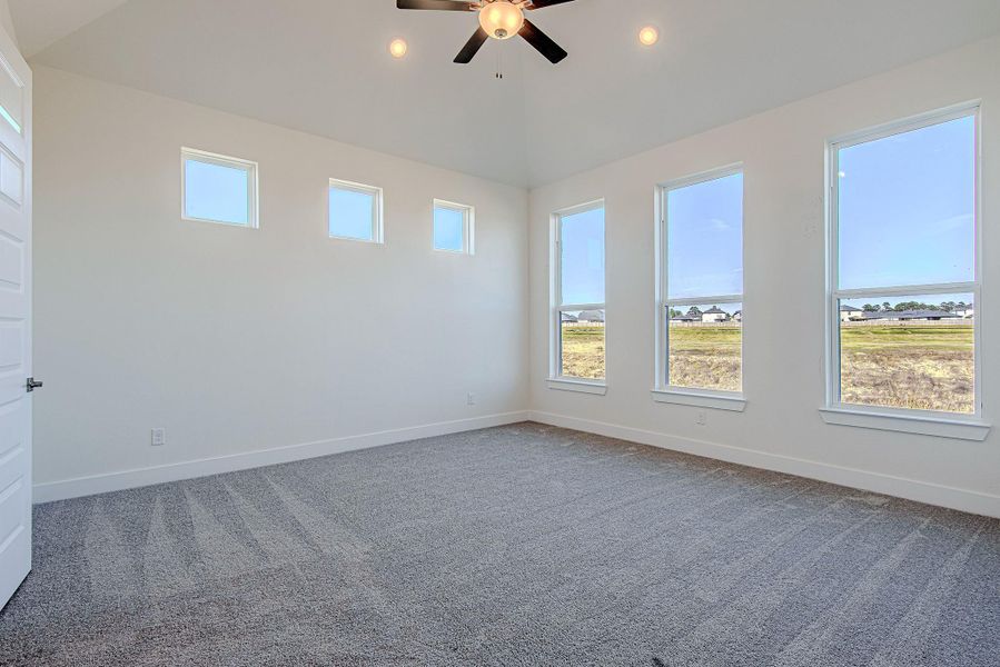 Primary bedroom featuring carpet flooring, ceiling fan, and large windows providing natural light.