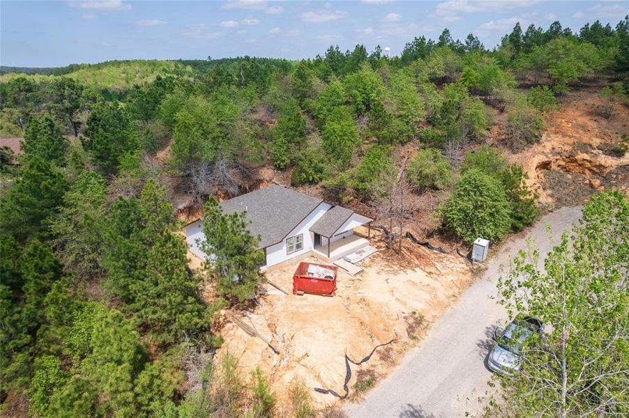 Aerial view of the property, featuring a white exterior and a gray roof, surrounded by extensive greenery and mature trees