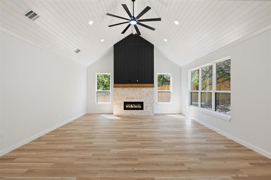 Unfurnished living room featuring ceiling fan, light wood-style floors, a lit fireplace, wood ceiling, and high vaulted ceiling Unfurnished living room featuring ceiling fan, light wood-style floors, a lit fireplace, wood ceiling, and high vaulted ceiling