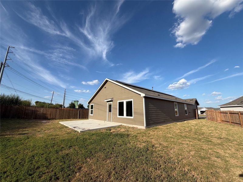 An expansive backyard patio connects seamlessly to the modern exterior under wide blue skies.