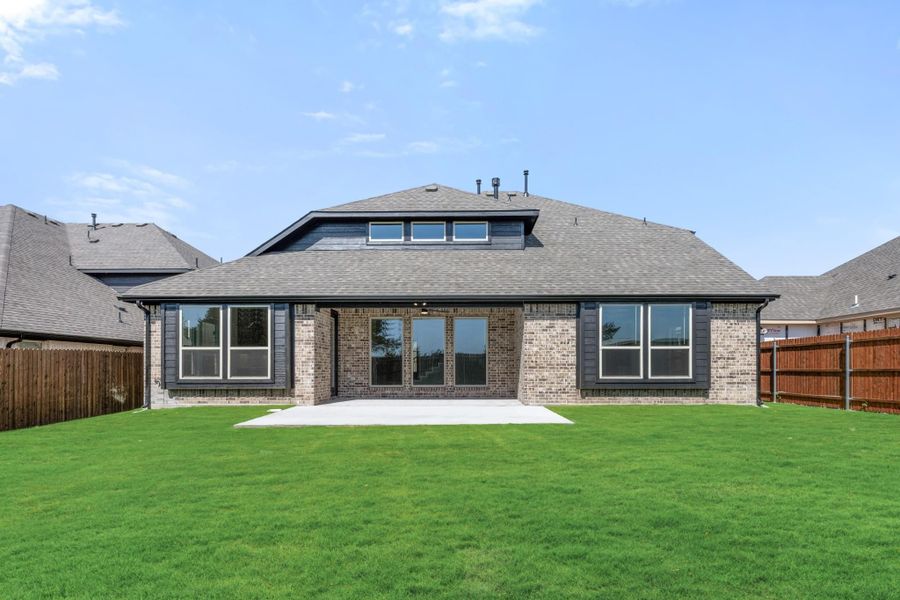 Rear exterior of brick home with large windows, concrete patio, and fenced green backyard Rear exterior of brick home with large windows, concrete patio, and fenced green backyard