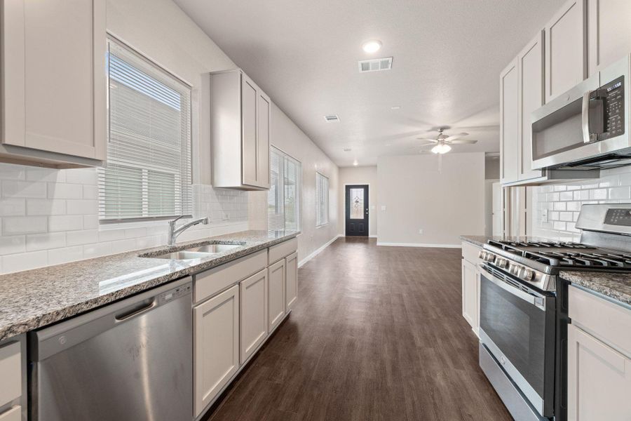 Kitchen featuring tasteful backsplash, appliances with stainless steel finishes, light stone countertops, dark wood-type flooring, and white cabinets