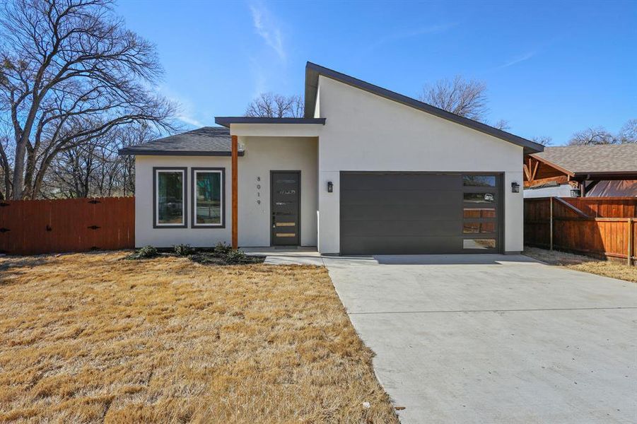 Modern home with a garage, concrete driveway, fence, and stucco siding