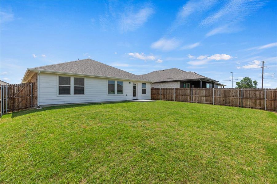 Expansive backyard featuring a lush lawn, privacy fencing, and a concrete patio