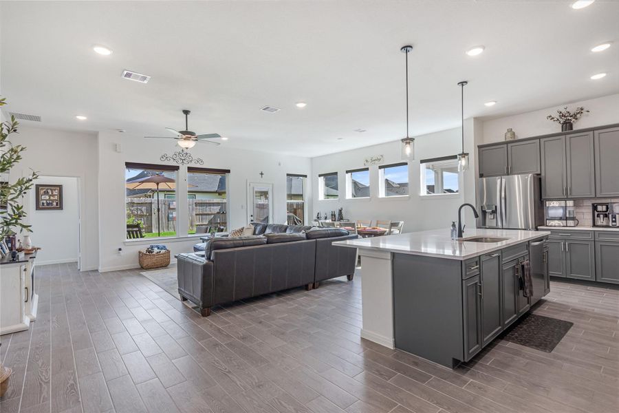 Spacious open-concept living area with elegant tile flooring, modern kitchen featuring a large island, stainless steel appliances, and ample natural light from large windows overlooking the backyard.