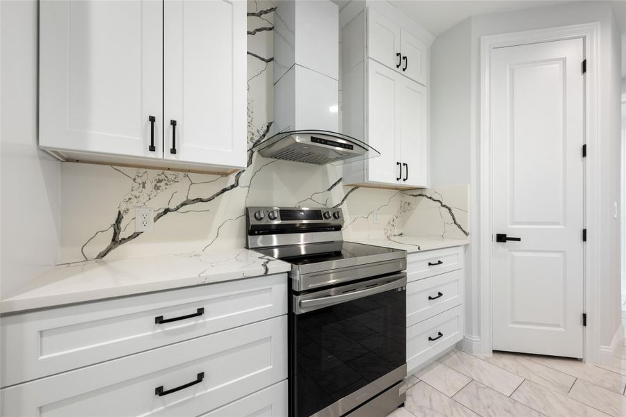 Kitchen featuring stainless steel electric range, white cabinetry, tasteful backsplash, and light stone counters
