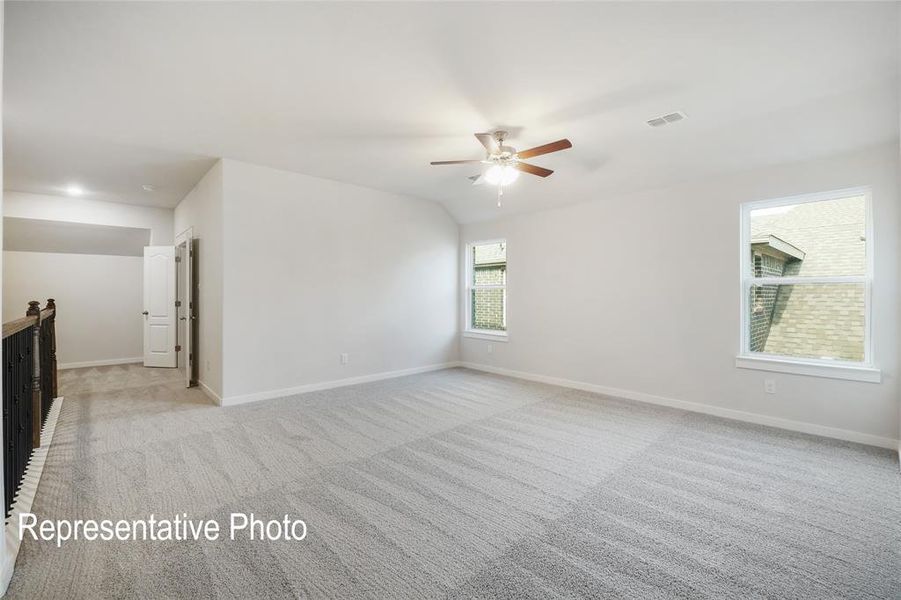 This spacious room features light-colored carpet, a ceiling fan, and multiple windows providing natural light