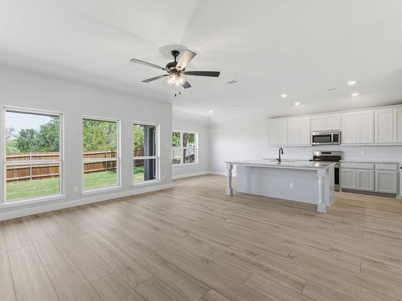 Open-concept living space featuring wood-finish flooring, a modern kitchen island with an undermount sink, stainless steel appliances, and a ceiling fan Open-concept living space featuring wood-finish flooring, a modern kitchen island with an undermount sink, stainless steel appliances, and a ceiling fan