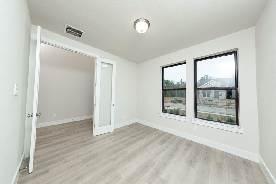 Tucked peacefully in the front of the home is this study, which features large windows, laminate flooring, French doors, and neutral toned walls.