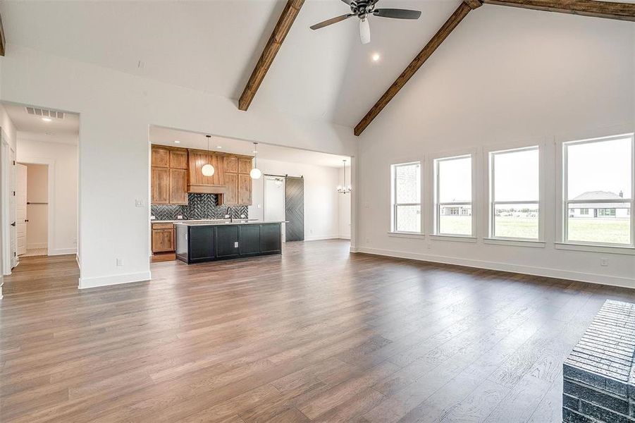 Unfurnished living room with hardwood / wood-style floors, a wealth of natural light, beam ceiling, high vaulted ceiling, and ceiling fan