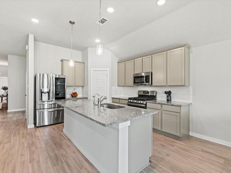 Modern island kitchen with granite counters, pendant lighting, and stainless appliances.