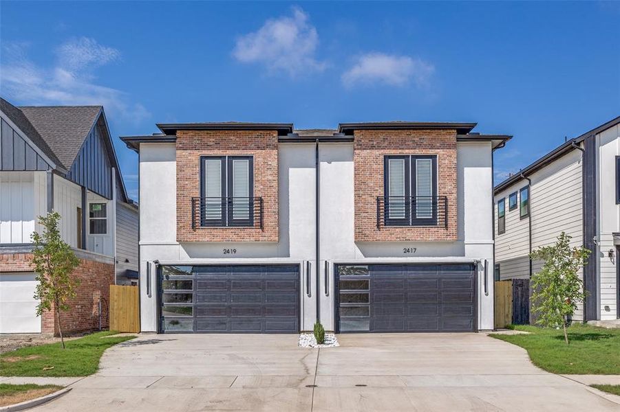 Contemporary home featuring concrete driveway, a garage, brick siding, and stucco siding Contemporary home featuring concrete driveway, a garage, brick siding, and stucco siding