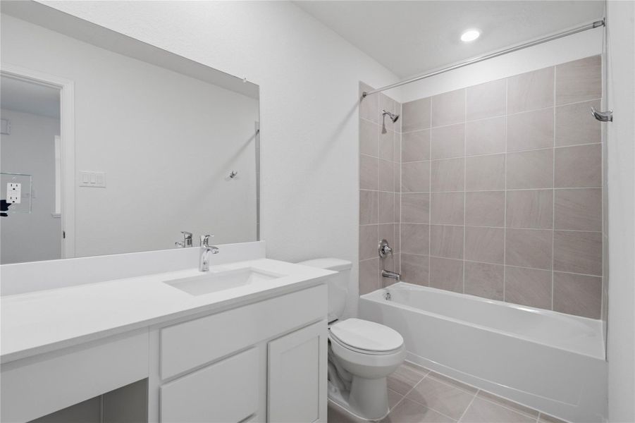 The secondary bathroom showcases tile flooring, a bath/shower combo with Daltile tile surround, vanity with knee space and a stunning light countertop, a stylish mirror, sleek fixtures, and contemporary finishes throughout.